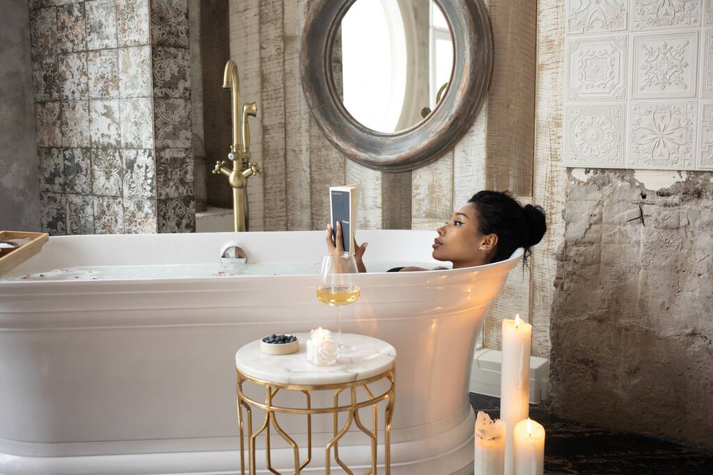A girl in a bathtub with candles reading a book